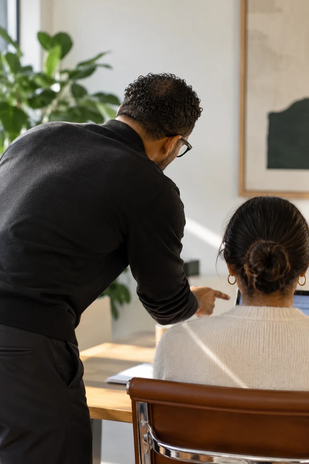 An advisor leaning in beside a leader, pointing at a plan on her laptop